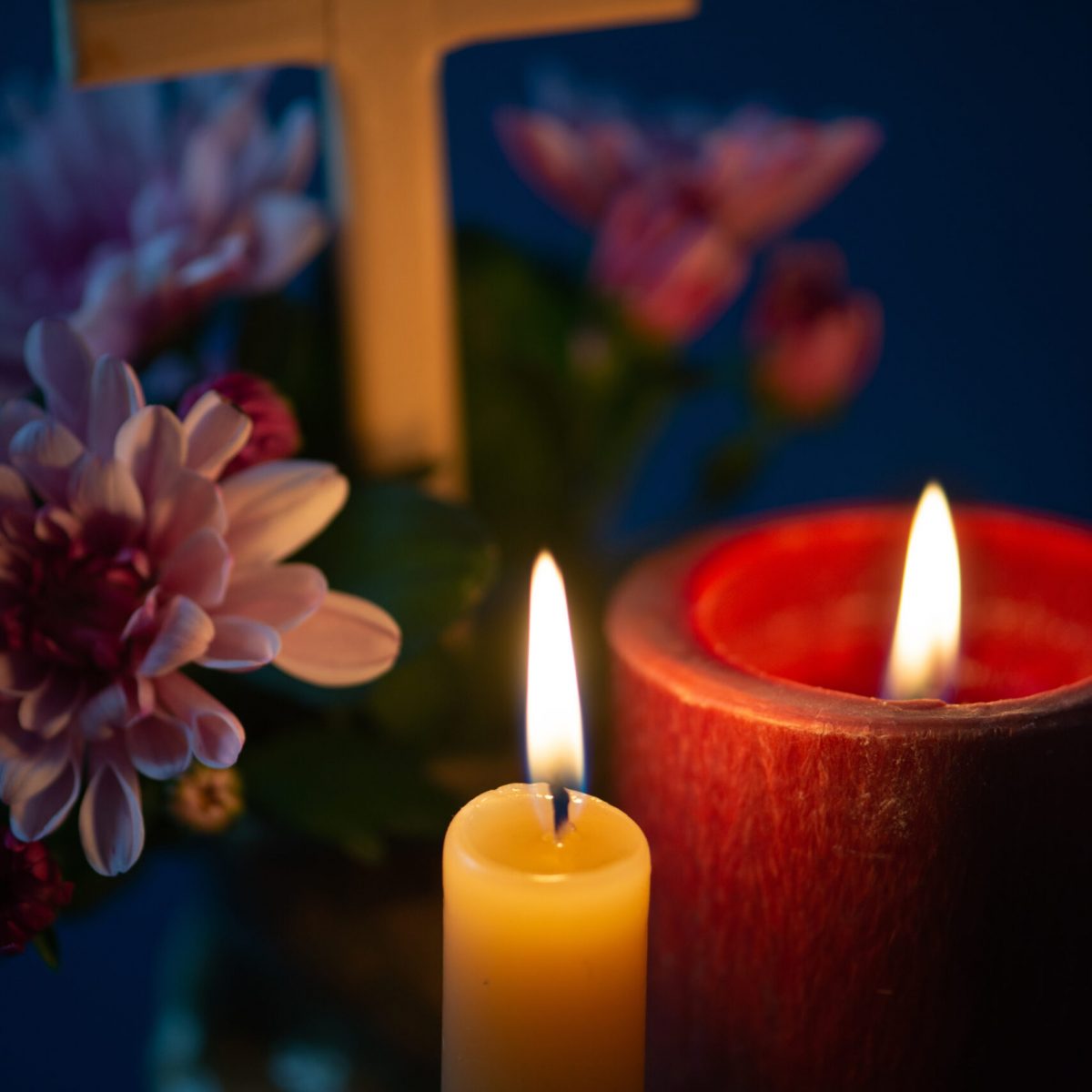 Composition of burning candle, flowers and wooden cross for all souls day. Also suitable for funeral, mourning, grief. Macro, selective focus.